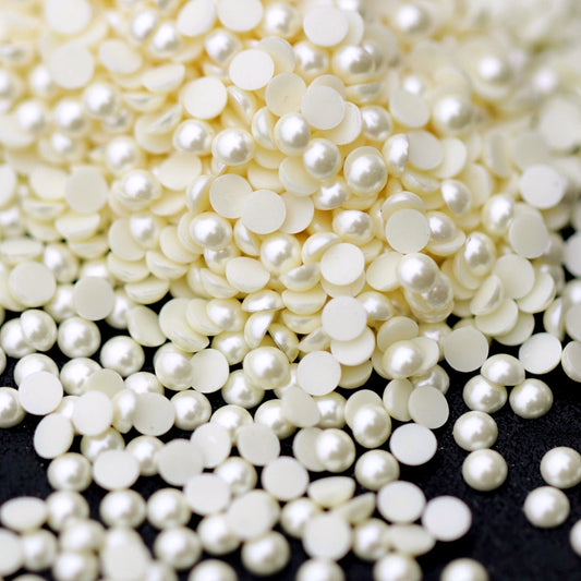A pile of small 2 mm eggshell acrylic half pearls scattered across a dark surface.