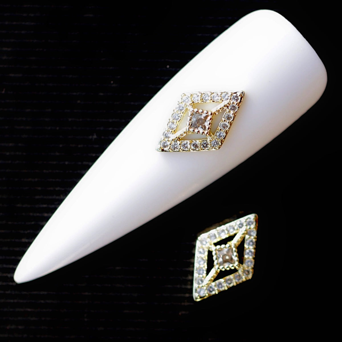 An approximately 13×8mm open rhombus-shaped Crystal CZ nail charm decorated with clear cubic zirconia stones and a larger central faceted crystal. The symmetrical geometric nail jewellery decoration features sparkling edges and gold-tone details, making it suitable for bridal manicures, French nails, glamour designs, evening looks and statement accent nail art.