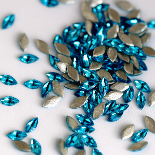 Flatback Zircon Nail Art Marquise crystals in Caribbean Blue, measuring 4×2mm. The elongated leaf-shaped crystals feature a precision-faceted surface with bright turquoise, aqua, cyan, ocean-blue and icy reflections. Ideal for tropical, ocean-inspired, floral, bridal and creative nail art designs.