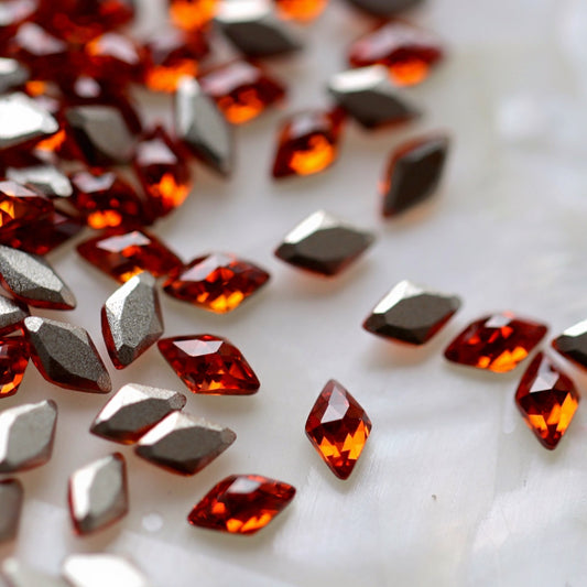Flatback Zircon Nail Art Rhombus crystals in Hyacinth, measuring 5×3mm. The diamond-shaped precision-faceted crystals feature bright orange-red, fiery coral, amber, vermilion and deep reddish-orange reflections. Ideal for autumn nails, flame-inspired designs, geometric nail art, festive manicures and luxury crystal arrangements.