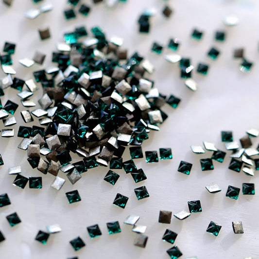 Flatback Zircon Nail Art Square crystals in Emerald, measuring 1.5mm. The tiny square-shaped crystals feature a faceted front surface with rich emerald green, forest green, jewel green and subtle teal reflections. Ideal for detailed nail art, geometric patterns, crystal borders, festive manicures and elegant nail decorations.