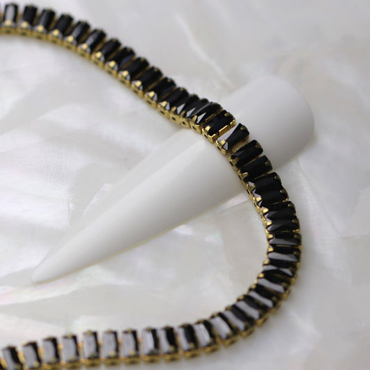 Close-up of gold cup chain with 4×2 mm jet zirconia baguette rhinestones displayed around a white nail tip