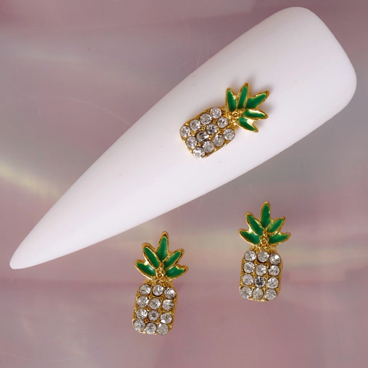 Tropical pineapple nail charm featuring a polished gold-tone outline, vivid green leaves and a pineapple body decorated with clear Crystal-coloured rhinestones. This glamorous summer decoration is ideal for tropical manicures, beach nail art, holiday designs and sparkling accent nails.