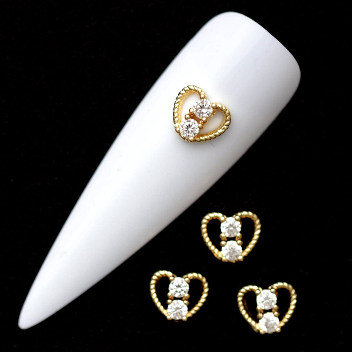 Gold 7×6 mm rope-style heart nail charms with two crystal CZ stones displayed on a white nail tip against a black background