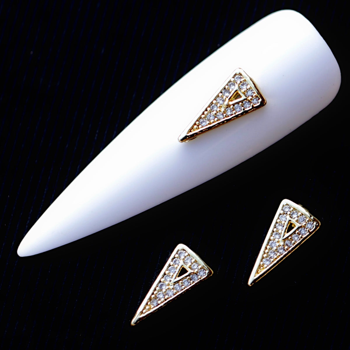 Elongated triangular nail charm with a shiny gold-tone finish and miniature transparent cubic zirconia crystals arranged across the surface. The charm features a pointed lower tip and a small open geometric detail in the centre, making it suitable for bridal manicures, geometric nail art, glamour designs and elegant accent nails.