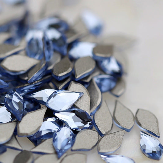 K9 Crystal Flatback Flame in Light Sapphire, measuring 6×3mm. The pointed flame-shaped crystal has a softly rounded lower body and a faceted front surface. Its transparent light-blue colour reflects icy blue, pale sapphire, aqua, sky blue, soft turquoise and silvery tones. Ideal for bridal nails, winter manicures, ocean-inspired nail art, floral designs, crystal clusters and elegant nail decorations.