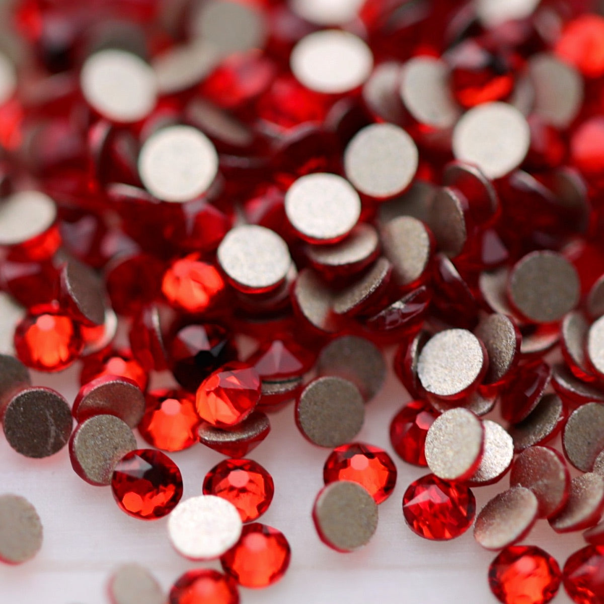 Close-up of round K9 flatback rhinestones in bright Light Siam red, showing sharp faceting and vivid scarlet and cherry-red reflections.