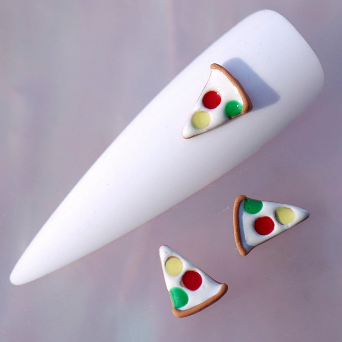 Pizza-shaped nail charm featuring a white pizza base, golden-brown crust and colourful red, yellow and green toppings. This playful food-themed nail decoration is ideal for novelty manicures, creative accent nails, party looks and colourful nail art designs.