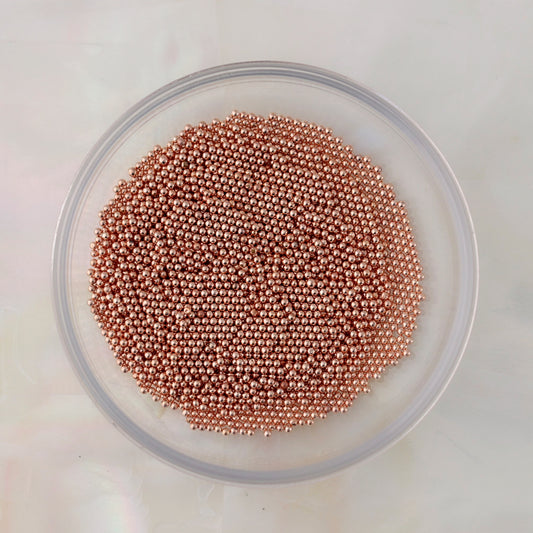 Close-up of small round rose gold metal caviar beads in several diameters for nail-art decoration.