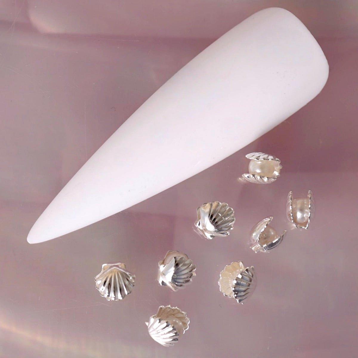 Silver seashell nail charm featuring ridged shell details and a small luminous pearl centre. This elegant ocean-inspired decoration is ideal for summer manicures, beach nail art, coastal designs, bridal manicures and mermaid-inspired accent nails.