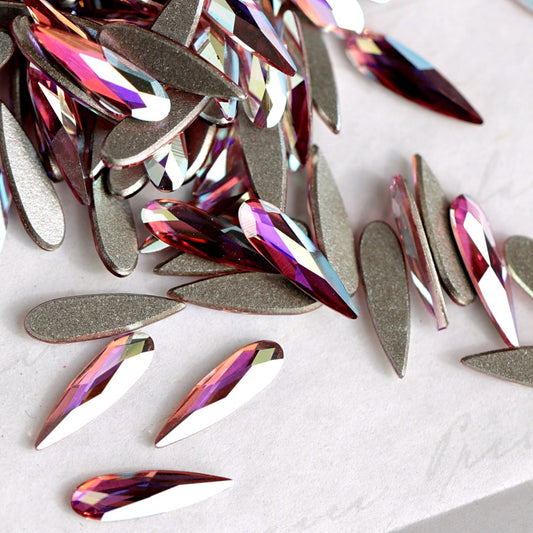 A pile of teardrop-shaped Swarovski 2304 Light Rose AB flatback rhinestones with a metallic silver backing, showing iridescent pink, purple, and blue reflections on a light gray background.