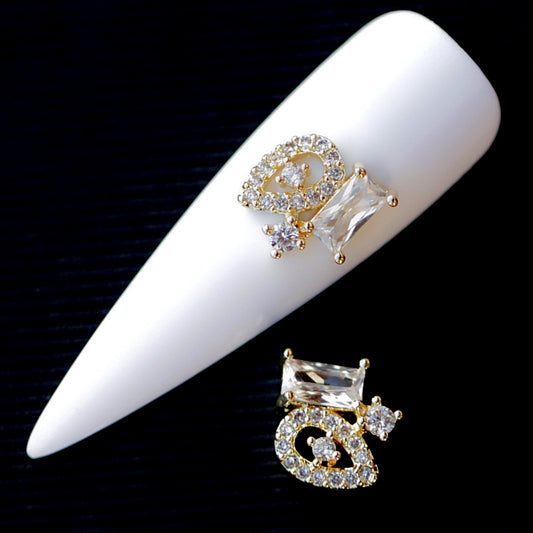 A 10×10mm multi-shape Crystal CZ nail charm set featuring a crystal-encrusted looped decorative element, a large clear faceted baguette-style stone, smaller round crystals and gold-tone details. The assembled nail jewellery decoration is suitable for bridal manicures, wedding nails, glamour designs, evening looks and statement accent nail art.