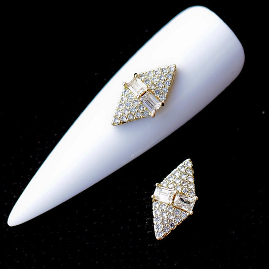 Rhombus-shaped Crystal CZ nail charm decorated with numerous clear cubic zirconia stones and two larger clear baguette-style crystals positioned across the centre. The diamond-shaped nail jewellery decoration features a sparkling surface and gold-tone details, making it suitable for bridal manicures, wedding nails, glamour designs, evening looks and statement accent nail art.