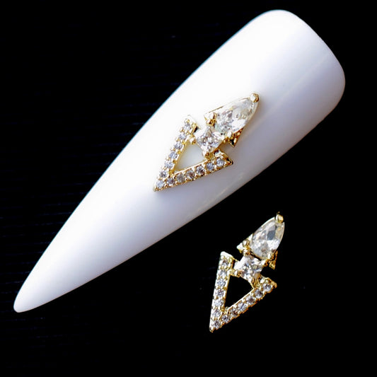 Crystal CZ triangle nail charm featuring an open triangular frame lined with clear cubic zirconia stones, a large faceted teardrop crystal at the top and a smaller round crystal in the centre. The gold-tone nail jewellery decoration is suitable for bridal manicures, wedding nails, glamour designs, evening looks and statement accent nail art.