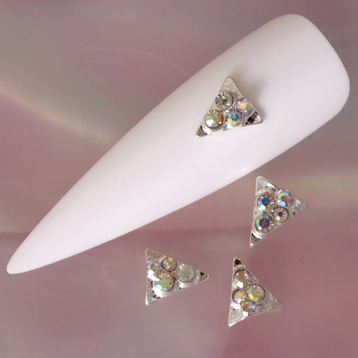 Geometric triangle nail charm featuring a polished silver-tone frame and multiple faceted clear and iridescent rhinestones. The crystals reflect flashes of pink, blue, green and gold, making this decoration ideal for geometric manicures, party looks, festival nail art and glamorous accent nails.