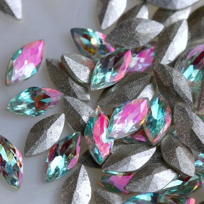 Faceted glass navette stones with a pale aqua-turquoise centre and luminous pink iridescent shimmer. The stones reflect mint, blue, lilac, silver and soft rainbow tones depending on the light. Their backs are slightly convex rather than completely flat, making them suitable for experienced nail artists creating floral, bridal, mermaid and detailed crystal nail-art compositions.
