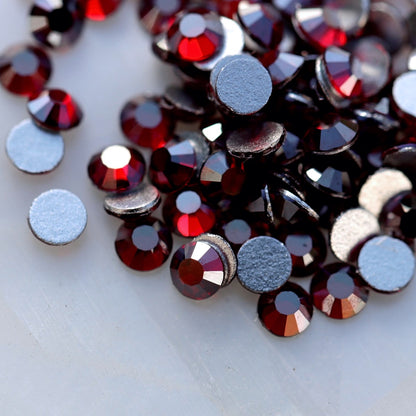 Faceted glass flatback rhinestones in a deep Dark Siam burgundy-red shade with a special metallic silver reflective shimmer visible from selected angles. The stones show rich dark ruby-red colour with cool silver, steel-grey and graphite-like flashes, making them ideal for gothic, Christmas, winter, party and dark romantic nail art.