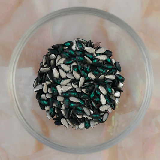 Glass bowl filled with Flatback Zircon Nail Art Drop Emerald crystals, showing many deep green teardrop stones with silver flatbacks ready for nail art and decorations.