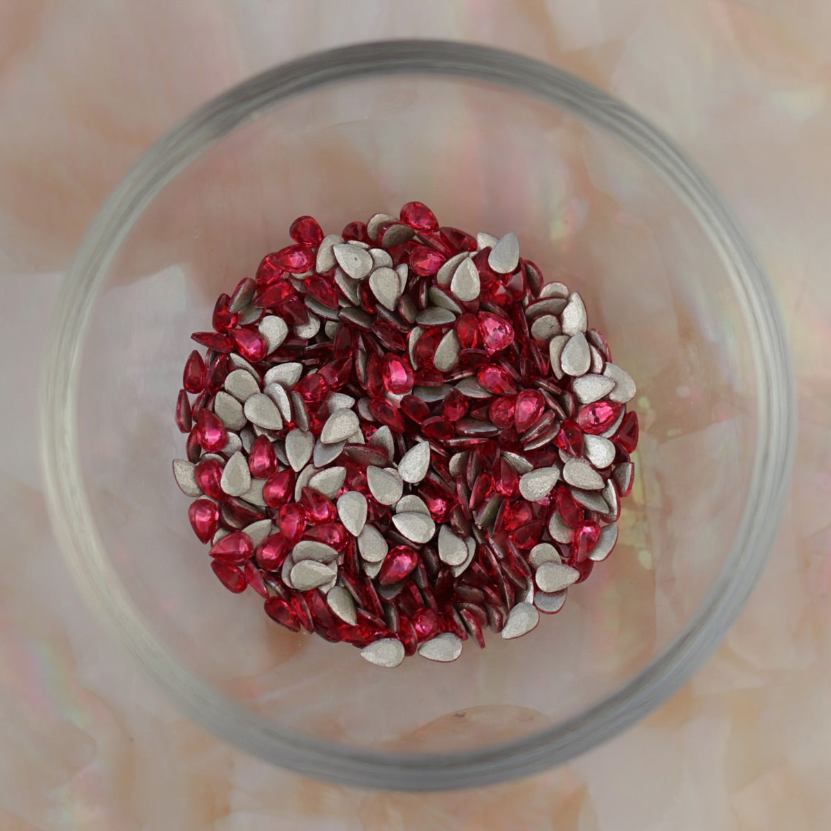 Glass bowl filled with Flatback Zircon Nail Art Drop Magenta crystals, showing many bright pink teardrop stones with silver flatbacks ready for nail art and decorations.
