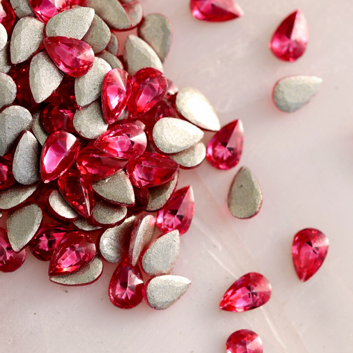 Flatback Zircon Nail Art Drop Magenta stones scattered on a light surface, displaying vivid pink teardrop crystals alongside their metallic foil backs.