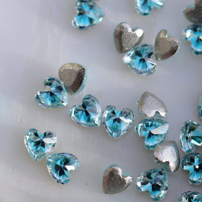 Close-up of faceted aquamarine heart-shaped zircon nail decorations showing their bright blue colour and sparkling cut surfaces.