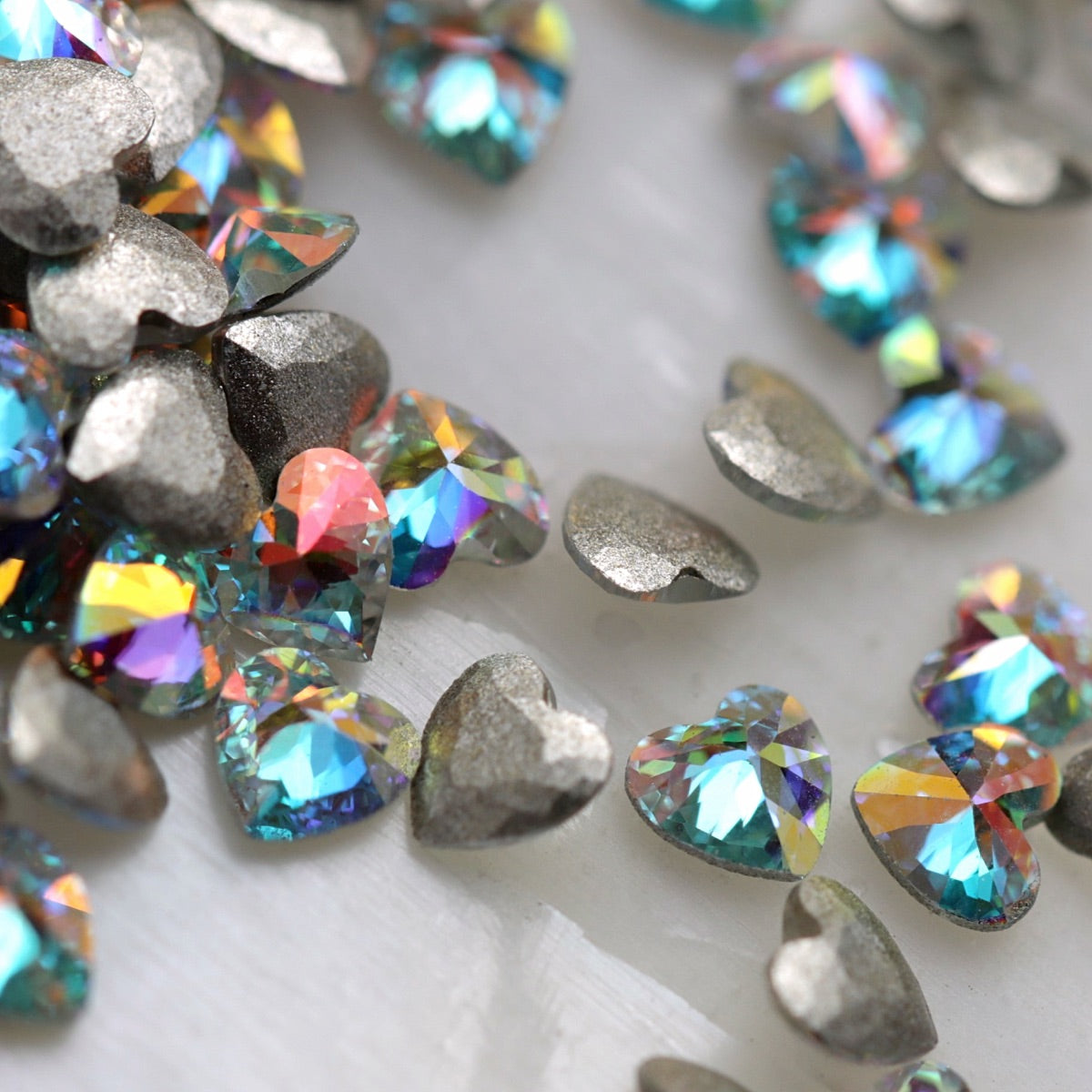 Crystal AB heart-shaped flatback zircon nail decorations shown from the front and back, highlighting their iridescent faceted surfaces and flat adhesive backs.
