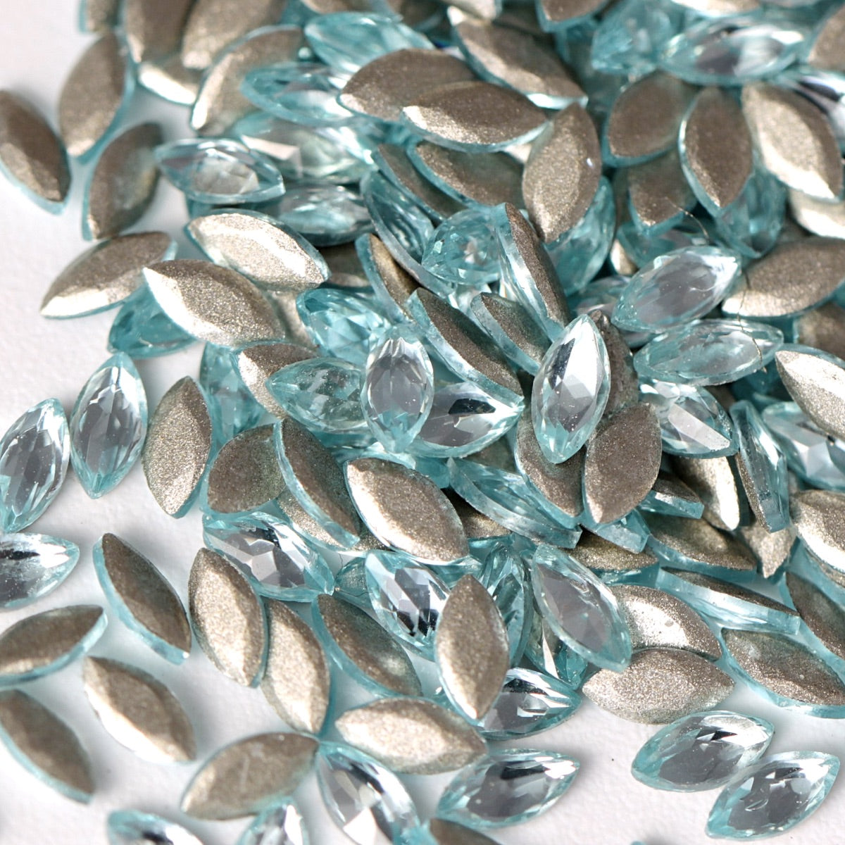 Aquamarine flatback zircon marquise rhinestones displayed in a detailed close-up. The elongated navette crystals feature a delicate icy-blue tone, sharp faceted cuts, and reflective foil backings that enhance their luminous sparkle. Perfect for creating elegant nail art, refined jewelry details, fashion embellishments, and decorative DIY designs.