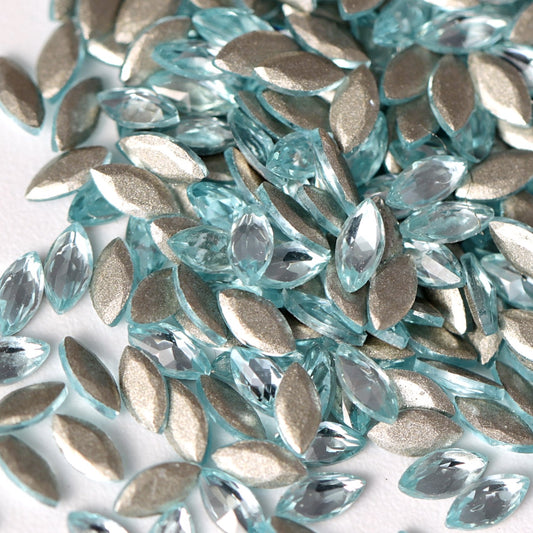 Aquamarine flatback zircon marquise rhinestones displayed in a detailed close-up. The elongated navette crystals feature a delicate icy-blue tone, sharp faceted cuts, and reflective foil backings that enhance their luminous sparkle. Perfect for creating elegant nail art, refined jewelry details, fashion embellishments, and decorative DIY designs.