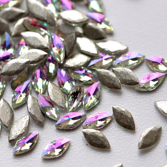 Flatback Zircon Nail Art Marquise crystals in Paradise Shine, measuring 4×2mm. The elongated leaf-shaped crystals feature a precision-faceted surface with shifting reflections in pink, magenta, purple, green, yellow, aqua, turquoise, blue and champagne tones. Ideal for floral, fantasy, festival, pastel and creative nail art designs.