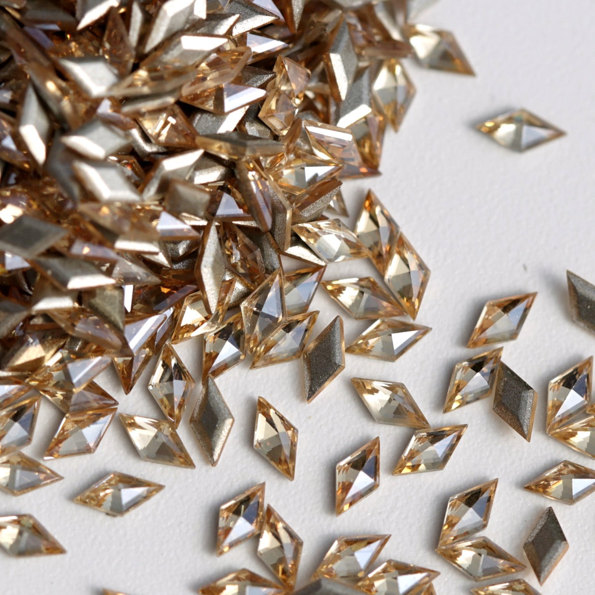 A detailed close-up of Light Peach rhombus-shaped zircon rhinestones displayed on a white background. Their warm, delicate peach color and sharply faceted surfaces reflect light beautifully, making them suitable for refined nail designs, jewelry accents, fashion decoration, and DIY creative projects.