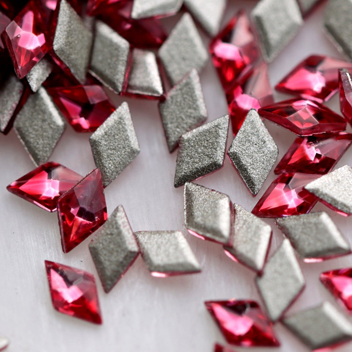 Close-up of 3.5×2mm Magenta faceted zircon rhombus stones, showing bright fuchsia, raspberry and deep red reflections with flat adhesive backs.