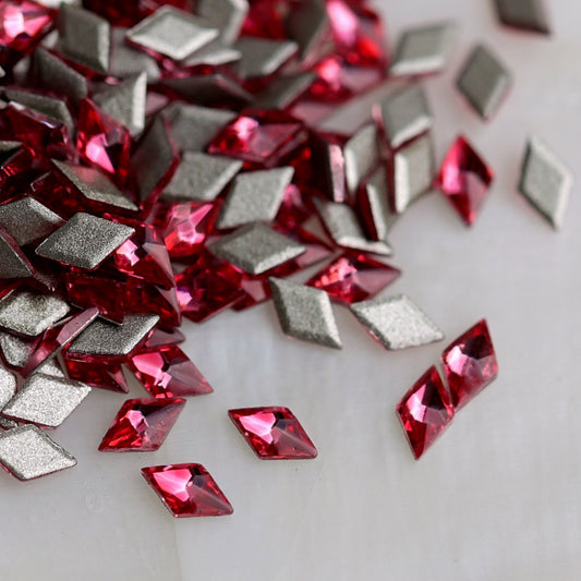 Magenta diamond-shaped flatback zircon nail-art stones displayed from the front and back, highlighting their slim geometric form, jewel-toned faceted surface and flatback design.