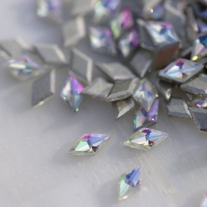 Close-up of slim 3.5×2mm rhombus zircon nail decorations in Paradise Shine, showing faceted surfaces with soft pink, purple, aqua and blue reflections.