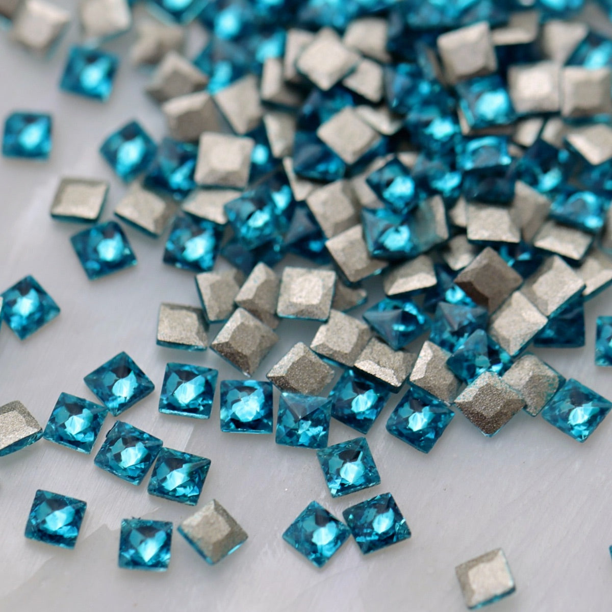 Caribbean Blue square zircon stones displayed from the front and back, highlighting their bright aqua-blue faceted surfaces and flatback design for nail-art application.