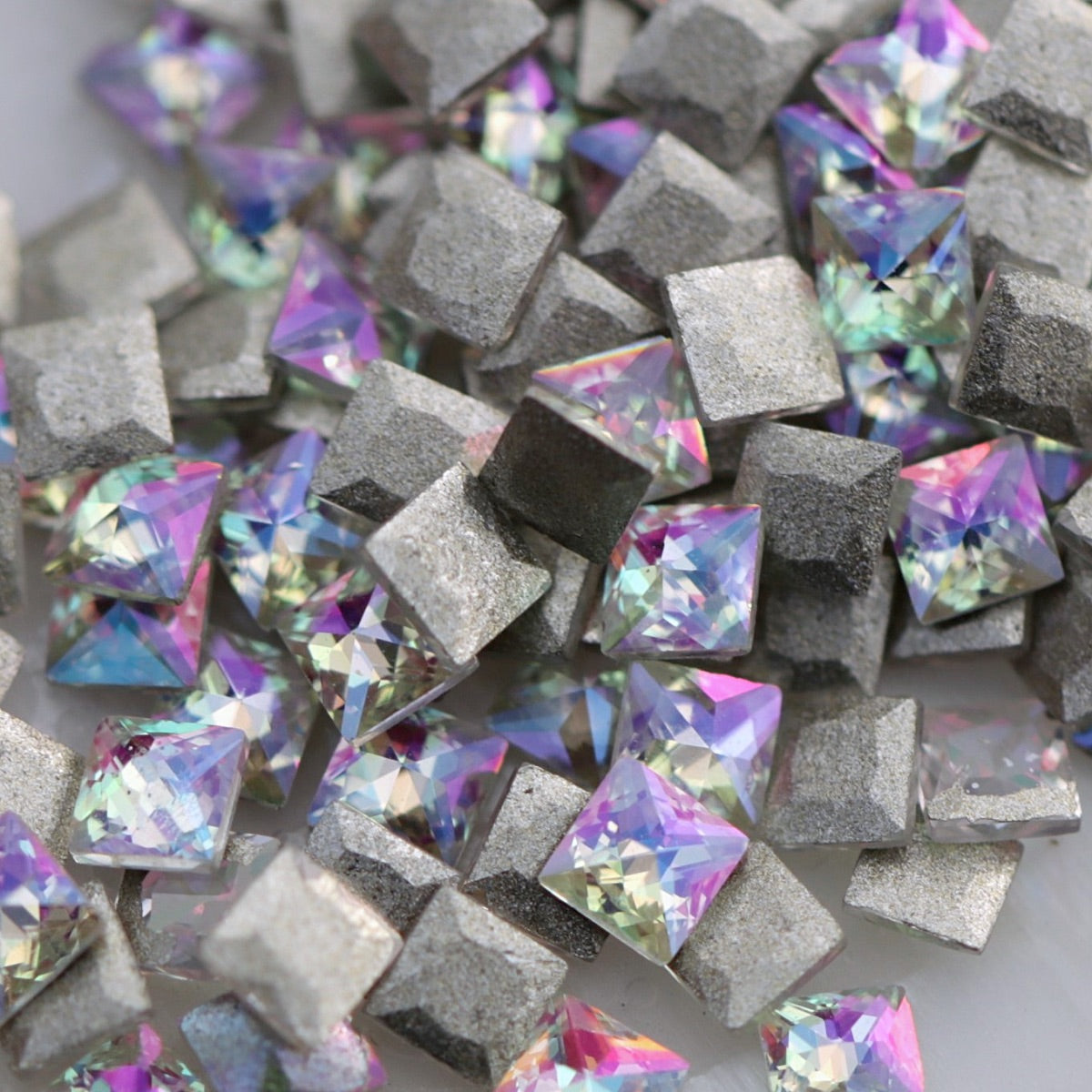 Close-up of faceted square zircon nail decorations in Paradise Shine, reflecting pink, purple, aqua, blue and green tones.