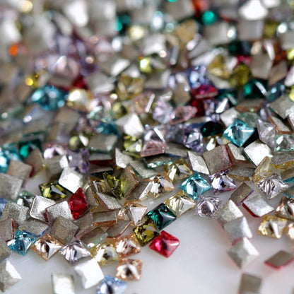 A close-up of tiny square flatback zircon stones in a range of colours, including aqua, blue, pink, red, green, yellow, purple and champagne. Their small size makes them suitable for detailed geometric nail art and precise decorative accents. The assortment is packed randomly, and colour quantities vary by package.