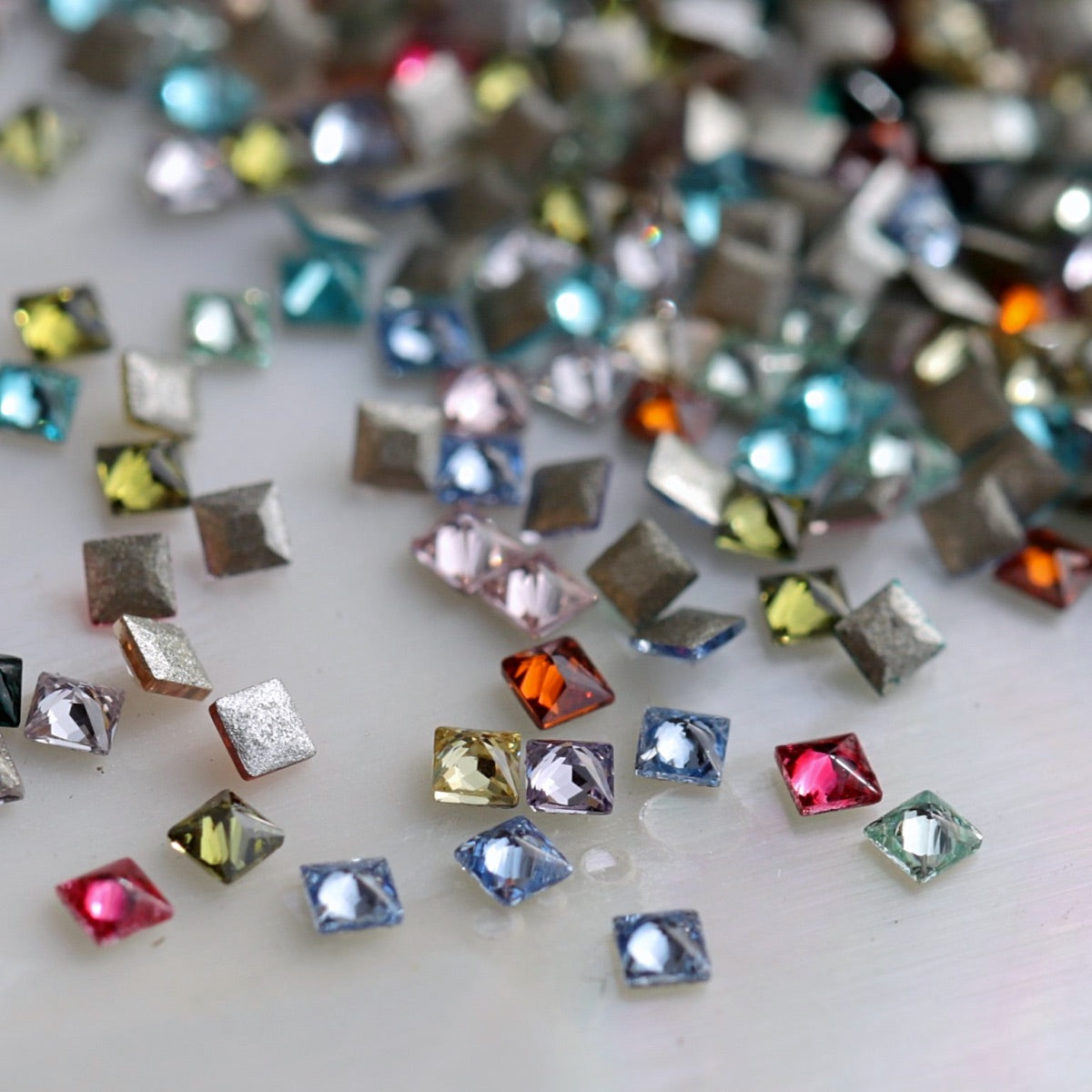 Close-up of mixed-colour 1.5mm square flatback zircon stones showing their faceted surfaces and assorted colours.