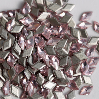 A detailed close-up of Light Rose rhombus-shaped zircon crystals arranged together with their reflective silver foil backings visible. The delicate pink color and sharp geometric facets add a sophisticated, multidimensional sparkle, making these crystals suitable for nail art, jewelry, accessories, and decorative craft projects.