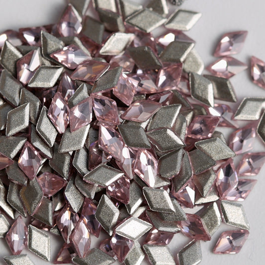 A detailed close-up of Light Rose rhombus-shaped zircon crystals arranged together with their reflective silver foil backings visible. The delicate pink color and sharp geometric facets add a sophisticated, multidimensional sparkle, making these crystals suitable for nail art, jewelry, accessories, and decorative craft projects.