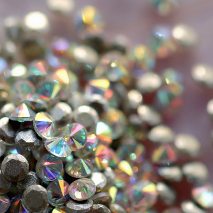 Pile of iridescent AB coated round Rivoli flatback zircon crystals showing rainbow sparkle on pearlescent pink background for nail art