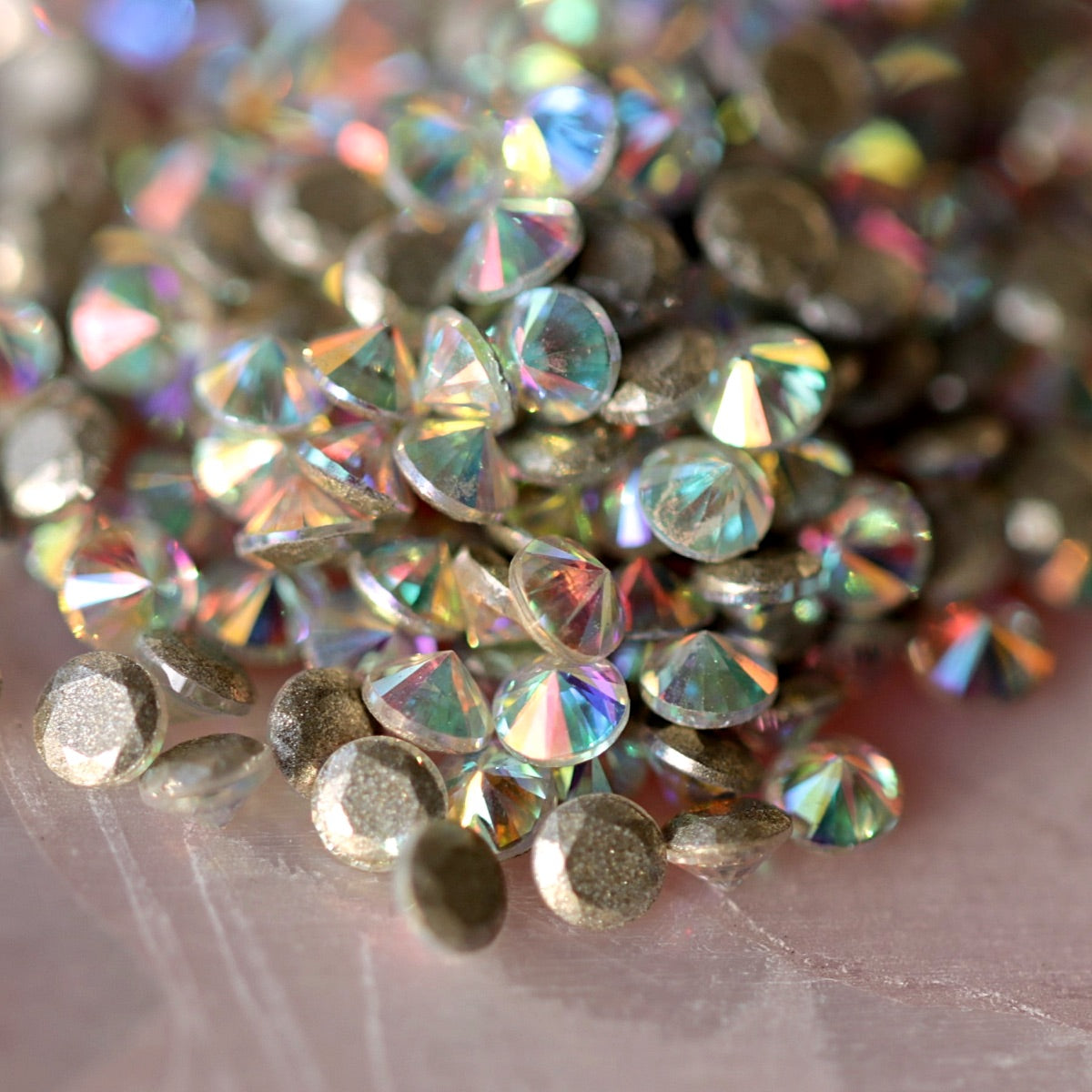 Scattered round AB zircons with multi-color reflections and metallic silver base on soft surface for dazzling nail embellishments