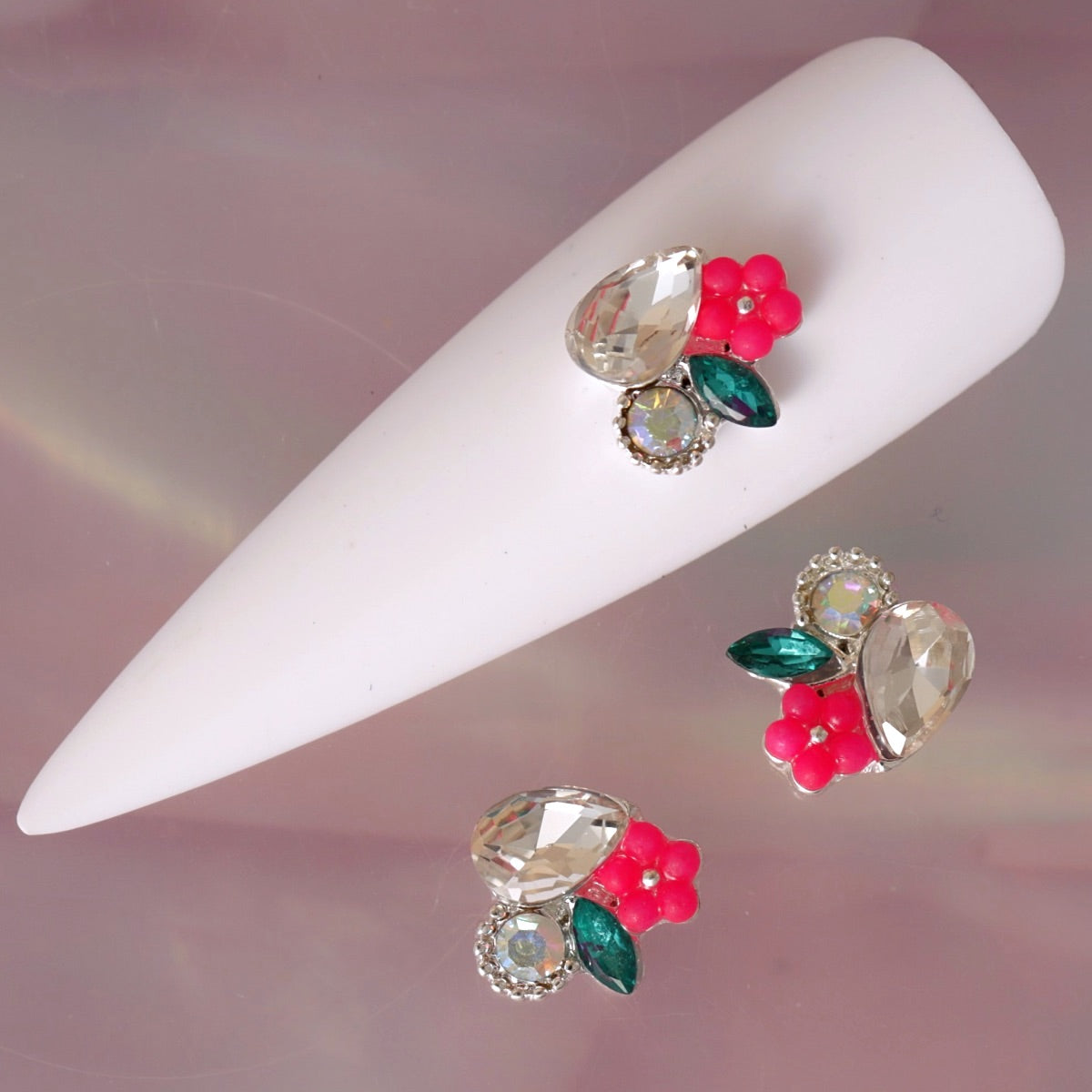 Floral nail charm featuring a large clear teardrop crystal, iridescent centre stone, bright pink flower, deep green leaf and silver-tone details. This elegant decoration is ideal for romantic manicures, floral nail art, bridal designs, summer looks and sparkling accent nails.