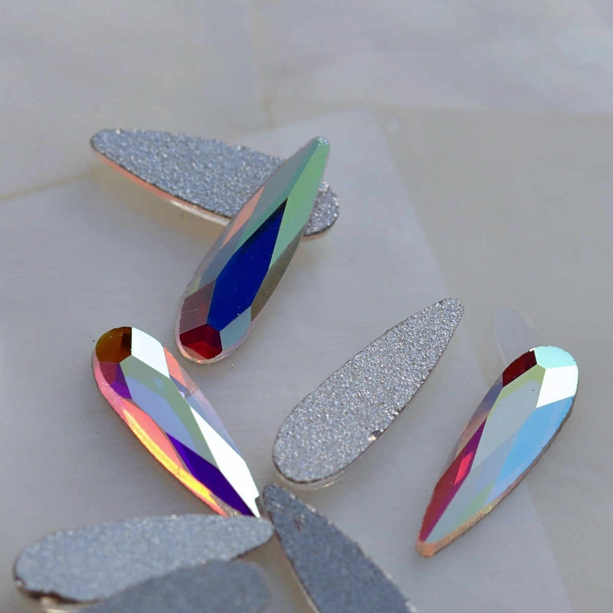 Crystal AB glass flatback raindrop with clear faceted surface and iridescent rainbow reflections.