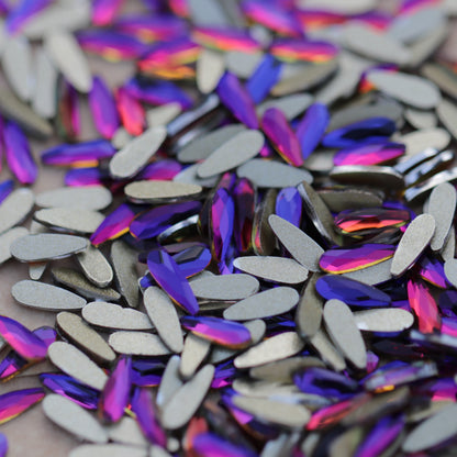 Slim flatback raindrop glass rhinestones in Meridian Blue showing blue, violet and pink reflections scattered on a surface.