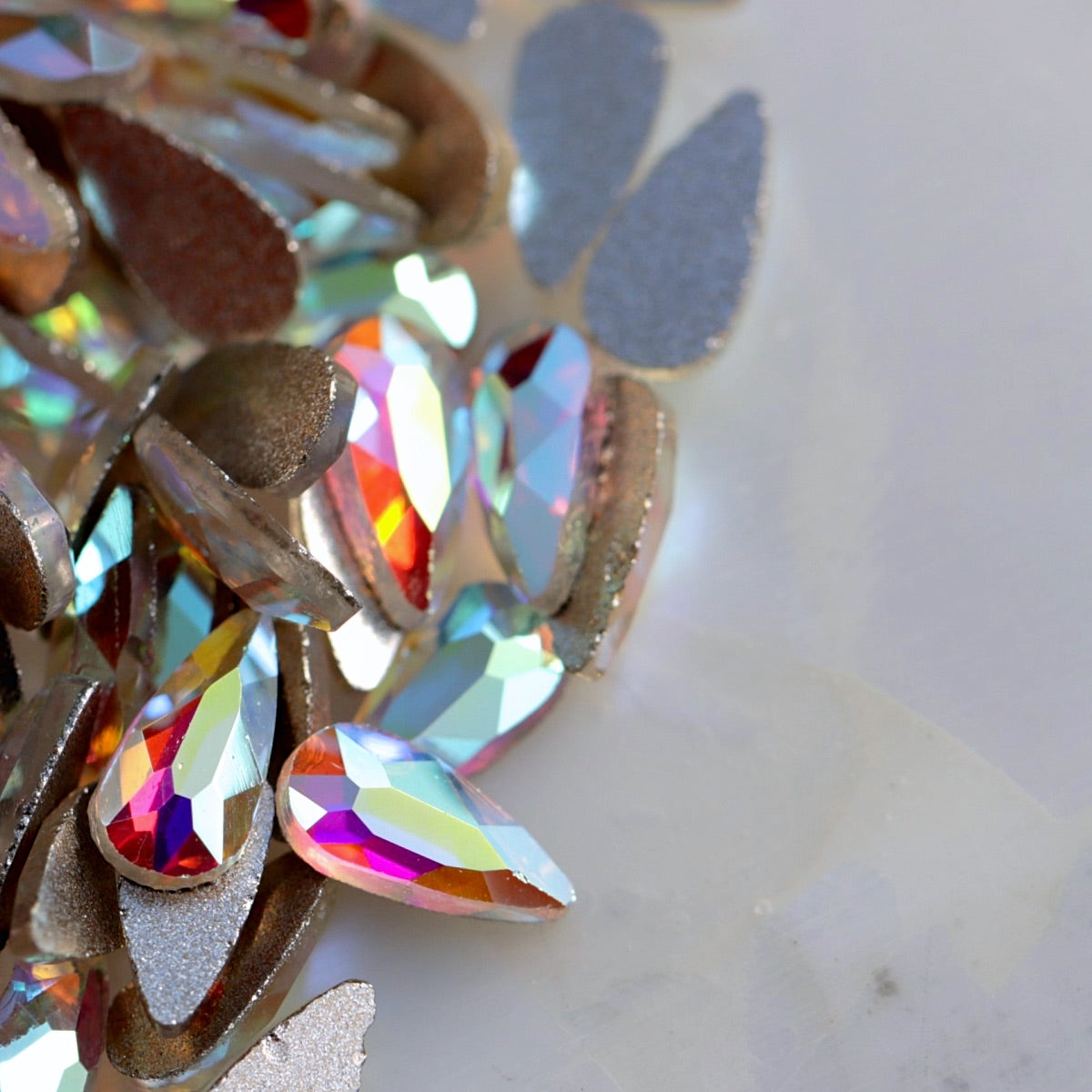 Crystal AB glass flatback teardrop with clear faceted surface and iridescent rainbow reflections.