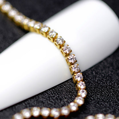 Gold 1.2 mm clear zirconia rhinestone nail art chain wrapped around a white nail tip on a black background