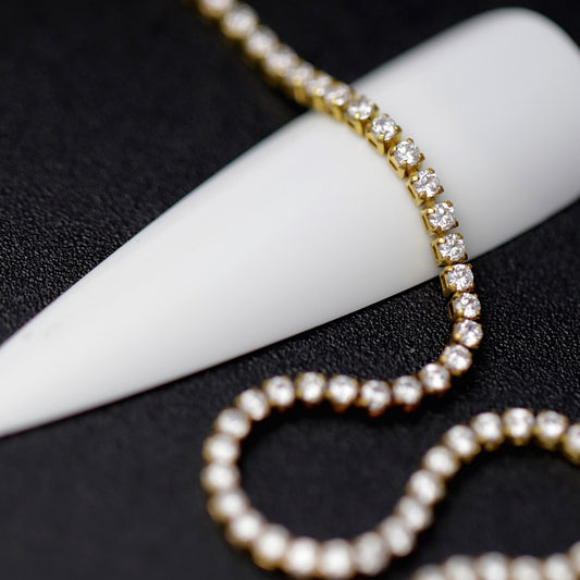 Gold 1.2 mm clear zirconia rhinestone nail art chain wrapped around a white nail tip on a black background
