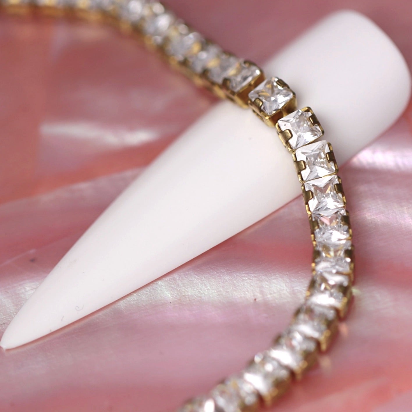 Gold cup chain with 3×3 mm clear zirconia square rhinestones wrapped around a white nail tip on a pink background