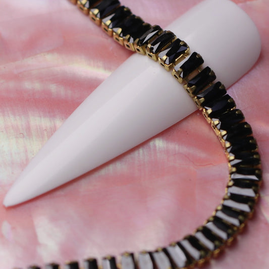 Gold 4×2 mm jet zirconia baguette rhinestone nail art chain wrapped around a white nail tip on a pink background