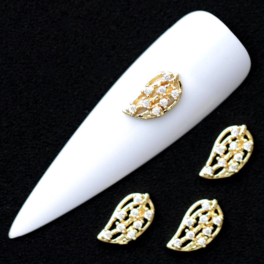 Gold 10×6 mm leaf-shaped nail charms with openwork design and mini crystal CZ stones displayed on a white nail tip against a black background